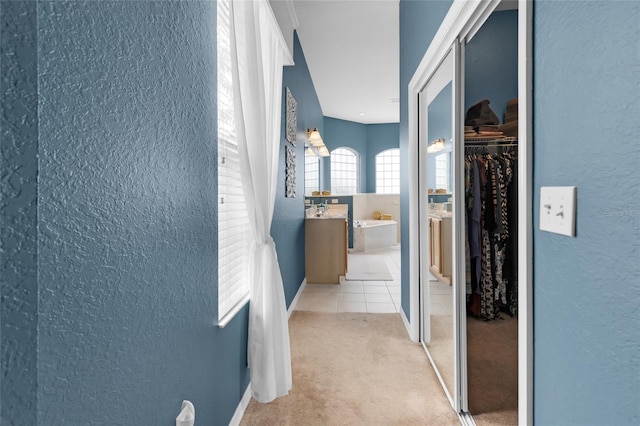 corridor featuring light tile patterned floors, a textured wall, baseboards, and light colored carpet