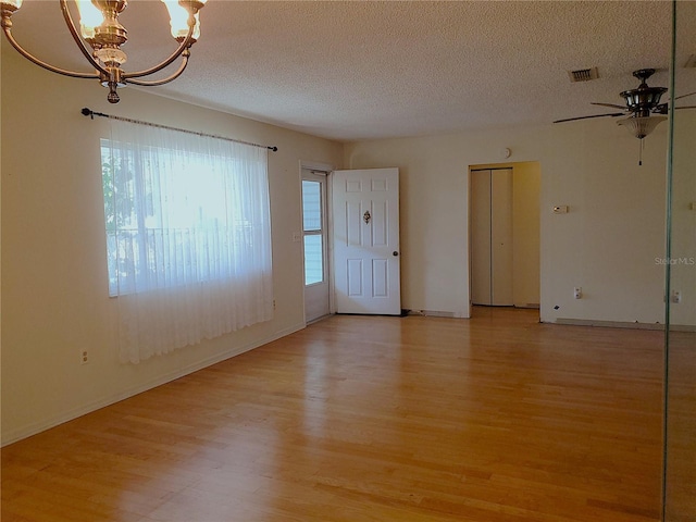 spare room with ceiling fan with notable chandelier, a textured ceiling, and light hardwood / wood-style floors