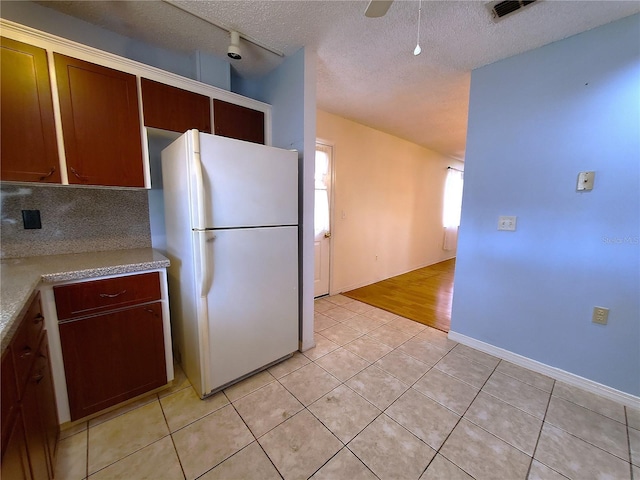 kitchen with light tile patterned floors, backsplash, a textured ceiling, and white refrigerator