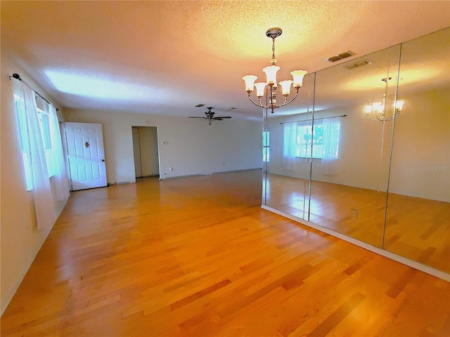 spare room featuring wood-type flooring, ceiling fan with notable chandelier, and a textured ceiling