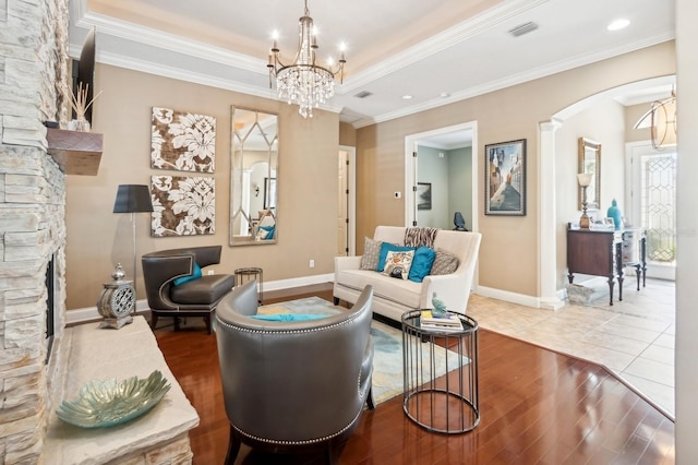 living room featuring ornamental molding, a stone fireplace, a chandelier, and light wood-type flooring