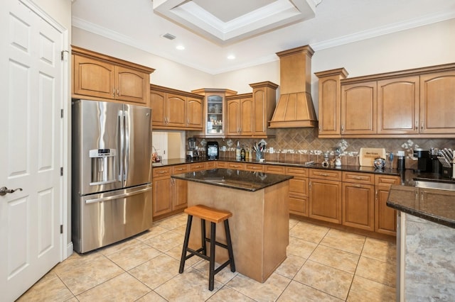 kitchen featuring stainless steel fridge, dark stone countertops, a kitchen breakfast bar, a center island, and custom exhaust hood