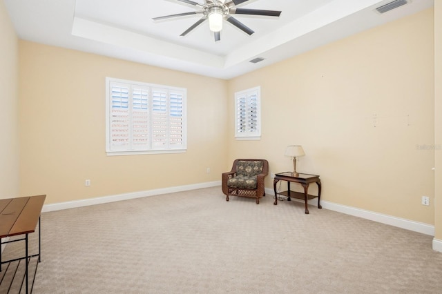 living area featuring a tray ceiling, light colored carpet, and ceiling fan