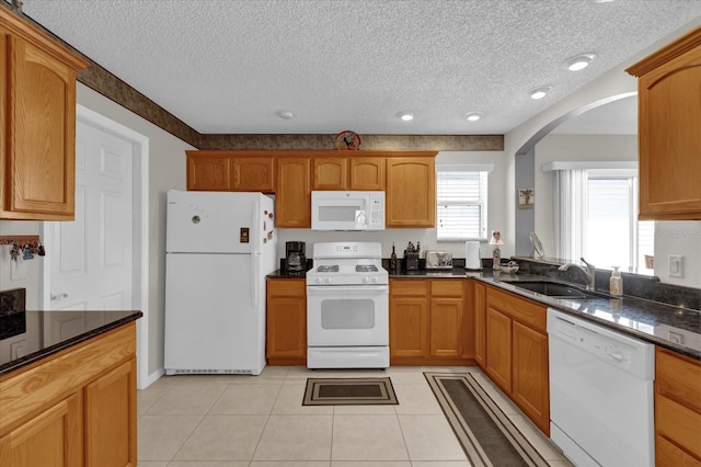 kitchen with sink, a textured ceiling, light tile patterned floors, white appliances, and dark stone counters