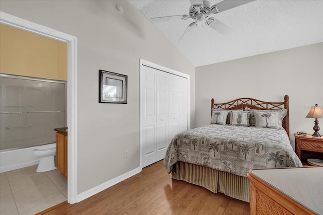 bedroom with connected bathroom, light hardwood / wood-style floors, a textured ceiling, vaulted ceiling, and a closet