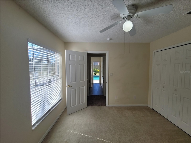 unfurnished bedroom with ceiling fan, light carpet, a textured ceiling, and a closet