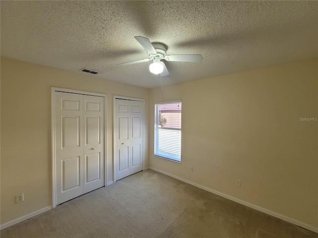 unfurnished bedroom featuring light carpet, two closets, a textured ceiling, and ceiling fan