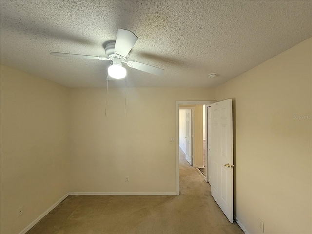 empty room featuring ceiling fan, light colored carpet, and a textured ceiling