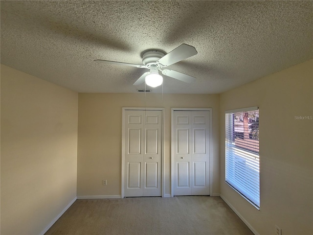 unfurnished bedroom featuring ceiling fan, a textured ceiling, light carpet, and two closets