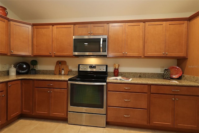 kitchen featuring stainless steel appliances, light tile patterned flooring, light stone countertops, and vaulted ceiling