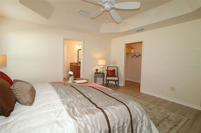 bedroom featuring a walk in closet, ceiling fan, light hardwood / wood-style floors, a raised ceiling, and a closet