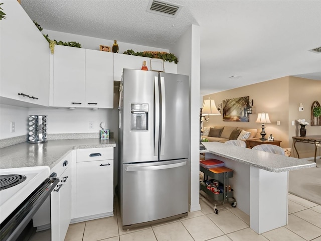 kitchen featuring light tile patterned floors, stainless steel fridge, white cabinetry, a textured ceiling, and kitchen peninsula