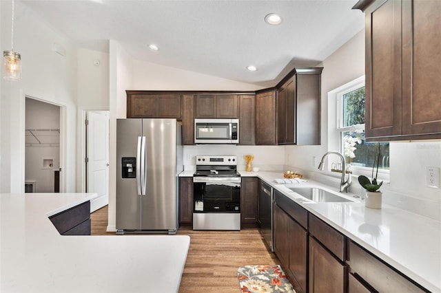 kitchen featuring dark brown cabinetry, stainless steel appliances, a sink, vaulted ceiling, and light countertops