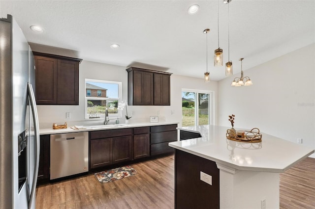 kitchen with sink, appliances with stainless steel finishes, dark brown cabinets, a kitchen island, and decorative light fixtures