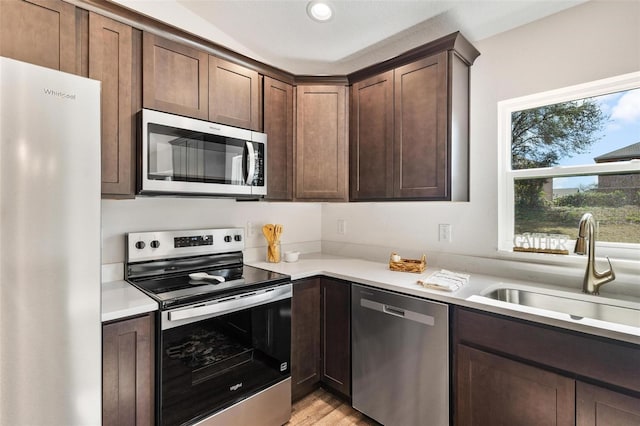 kitchen with appliances with stainless steel finishes, light countertops, a sink, and dark brown cabinetry