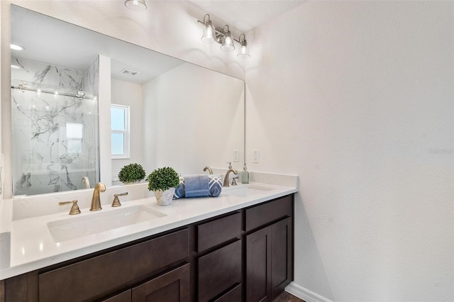 full bathroom with double vanity, a marble finish shower, baseboards, and a sink