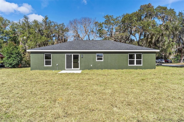 rear view of property with a shingled roof, a yard, and stucco siding