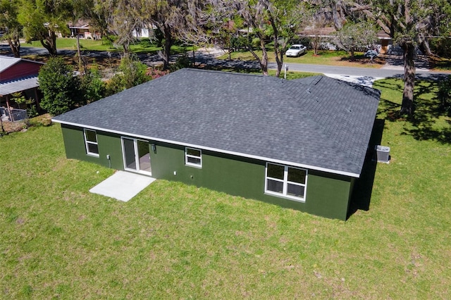 view of front of house featuring central AC unit, roof with shingles, a front yard, and stucco siding