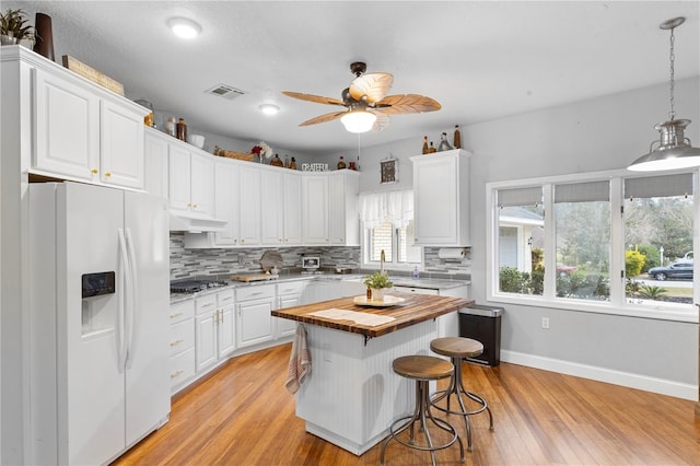 kitchen with visible vents, backsplash, white fridge with ice dispenser, white cabinets, and butcher block counters