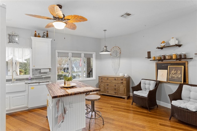 kitchen featuring visible vents, a sink, white dishwasher, light wood finished floors, and wooden counters