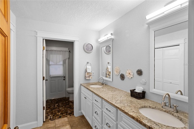 full bath with a textured ceiling, double vanity, toilet, and a sink