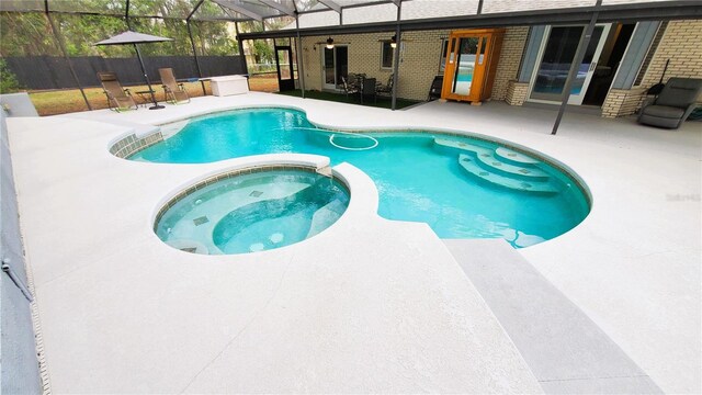 view of swimming pool with glass enclosure, a patio, fence, and a pool with connected hot tub