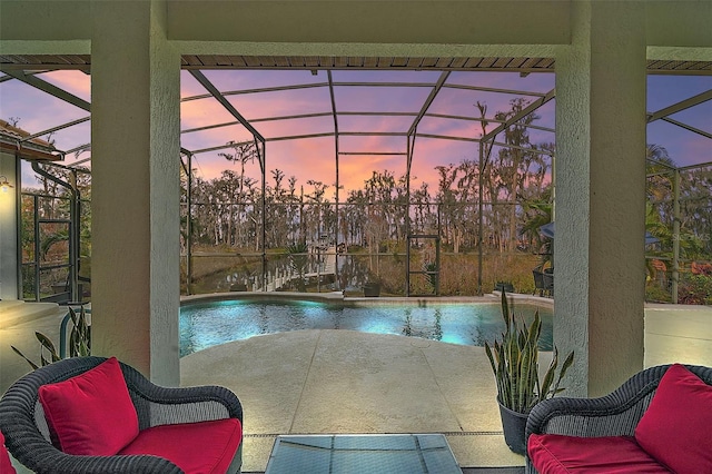 pool at dusk featuring glass enclosure and a patio