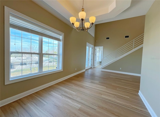 spare room featuring a notable chandelier, a tray ceiling, and light hardwood / wood-style flooring