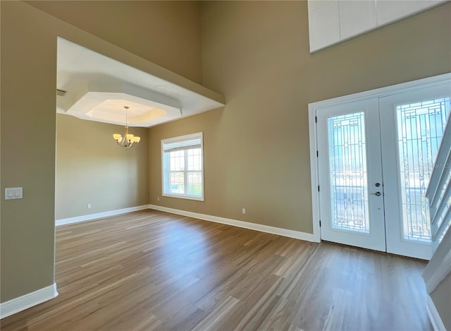 foyer featuring french doors, a raised ceiling, light hardwood / wood-style floors, and a notable chandelier