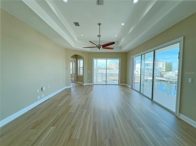 empty room with ceiling fan, light hardwood / wood-style floors, and a tray ceiling