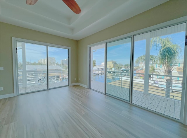 unfurnished room featuring ceiling fan, a tray ceiling, and light hardwood / wood-style flooring