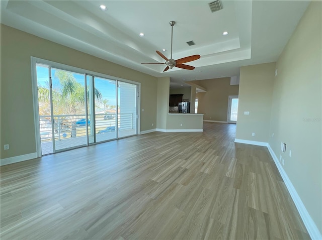 unfurnished living room with ceiling fan, light hardwood / wood-style floors, and a tray ceiling