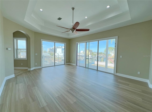 empty room featuring a raised ceiling, ceiling fan, and light wood-type flooring