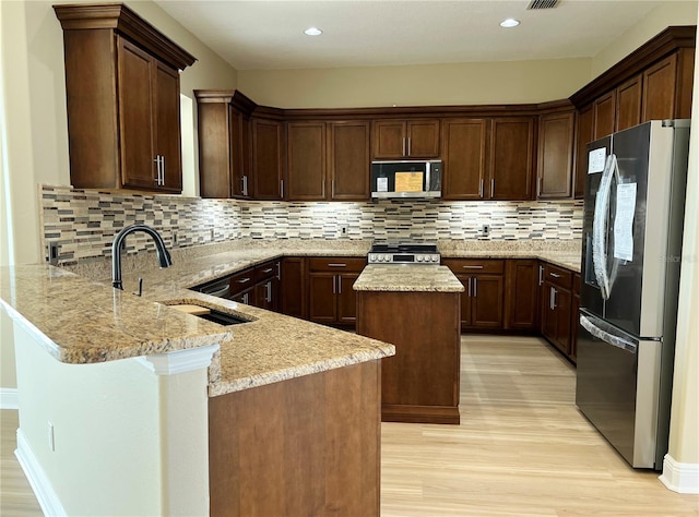 kitchen with sink, stainless steel fridge, range, light stone counters, and kitchen peninsula