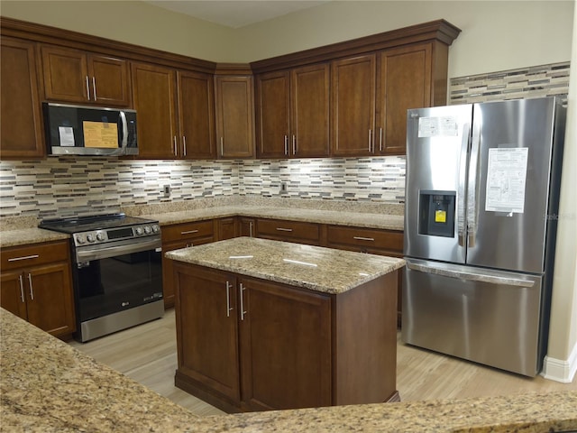 kitchen with light stone counters, appliances with stainless steel finishes, light hardwood / wood-style floors, and decorative backsplash