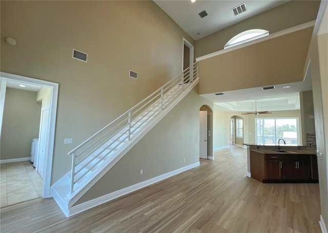 unfurnished living room featuring ceiling fan, sink, light wood-type flooring, and a high ceiling