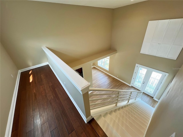 stairs with a towering ceiling, hardwood / wood-style floors, and french doors