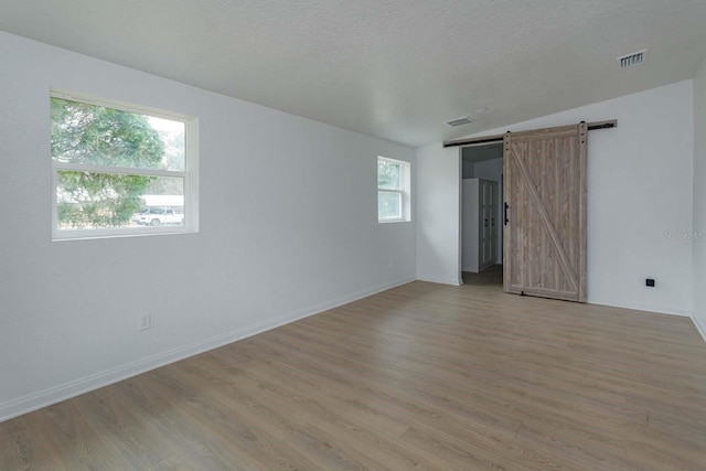 unfurnished room featuring light hardwood / wood-style flooring, a barn door, and a textured ceiling