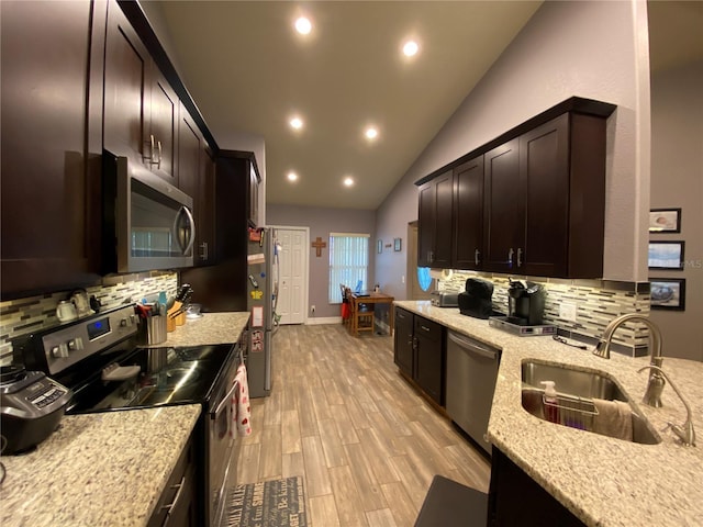 kitchen with sink, stainless steel appliances, light stone countertops, vaulted ceiling, and light wood-type flooring