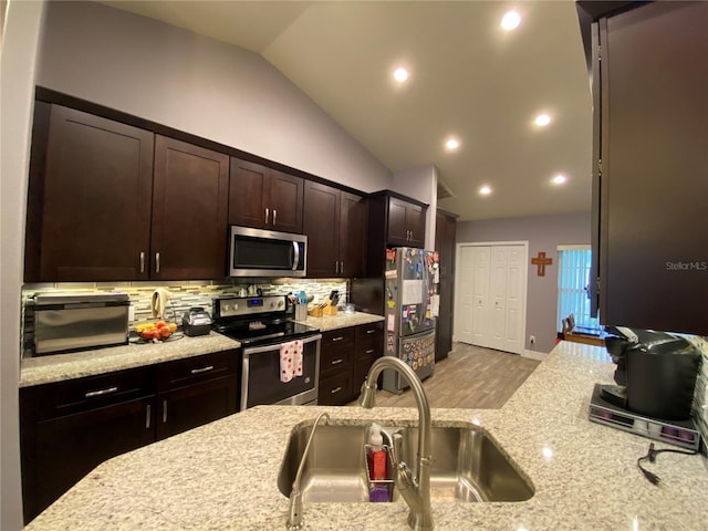 kitchen with sink, appliances with stainless steel finishes, backsplash, light stone counters, and vaulted ceiling