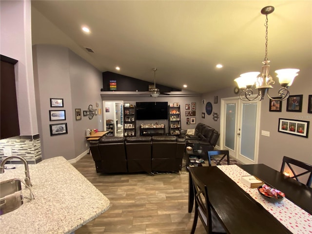 dining space featuring vaulted ceiling, ceiling fan with notable chandelier, sink, and hardwood / wood-style floors