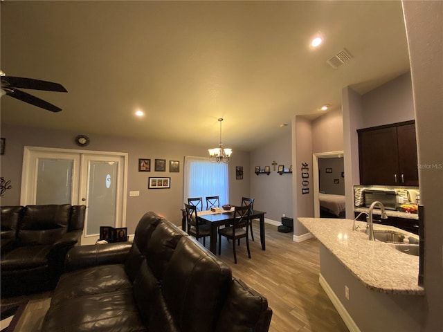 living room featuring sink, ceiling fan with notable chandelier, vaulted ceiling, and light wood-type flooring