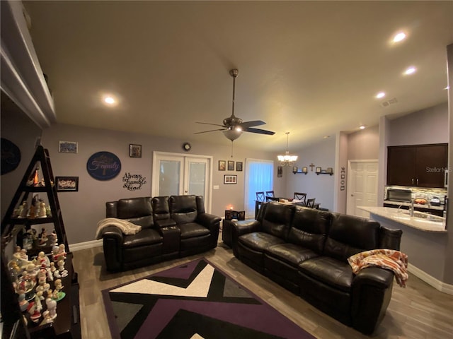 living room with ceiling fan with notable chandelier, vaulted ceiling, and light wood-type flooring