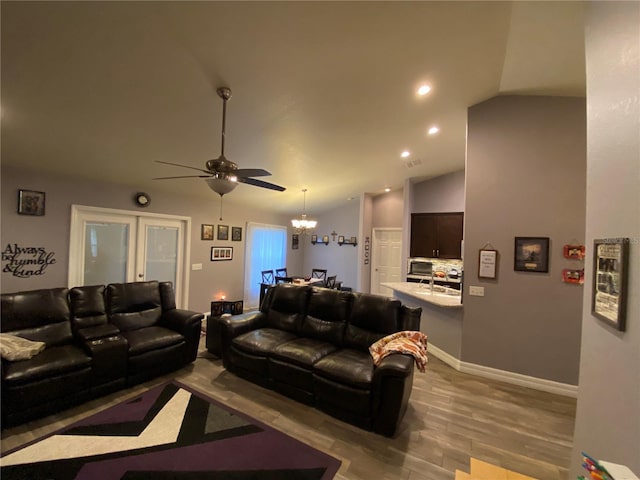 living room with lofted ceiling, sink, ceiling fan with notable chandelier, and light hardwood / wood-style flooring