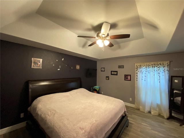 bedroom with a raised ceiling, hardwood / wood-style flooring, and ceiling fan