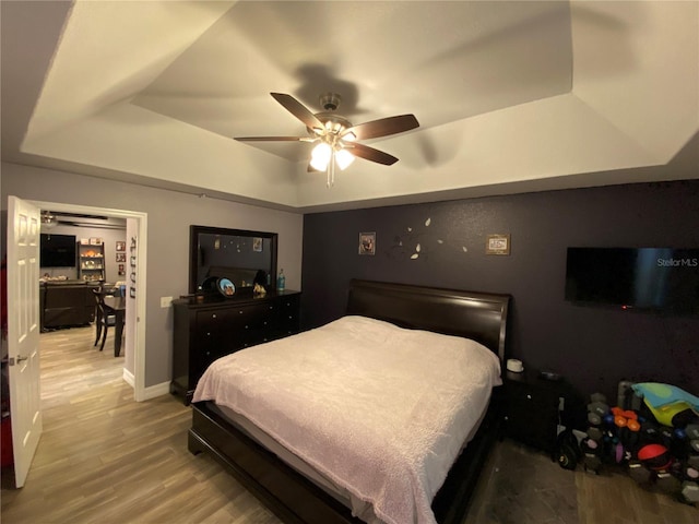 bedroom featuring ceiling fan, a raised ceiling, and light wood-type flooring