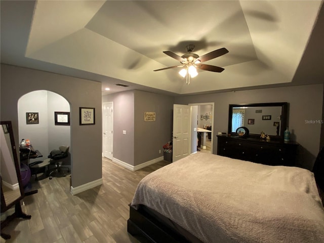 bedroom with a raised ceiling, hardwood / wood-style flooring, and ceiling fan