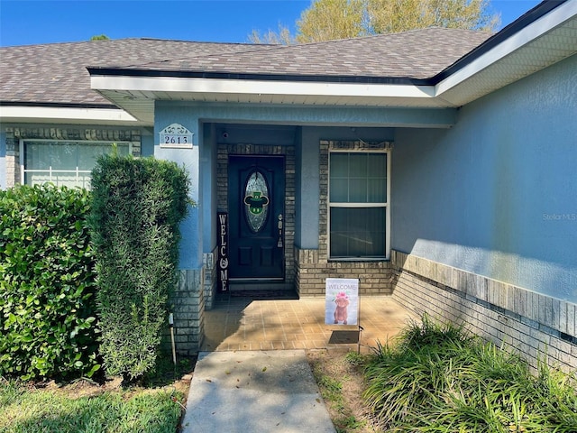 property entrance featuring a shingled roof and stucco siding