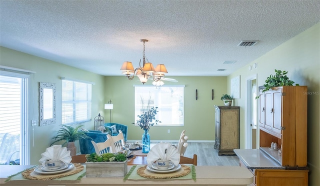 dining space featuring a textured ceiling, an inviting chandelier, visible vents, and light wood-type flooring