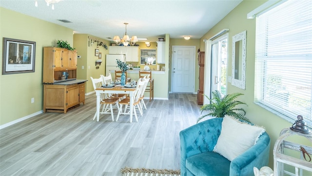 dining space with light wood-type flooring, visible vents, baseboards, and a chandelier